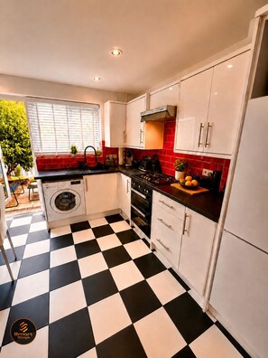 A kitchen with a black and white checkered floor, white cabinets, a built-in oven, and a washing machine. - Stylish 2-Bed Bedford Home | Sleeps 4 + Sofa Bed | Free Parking |Super Fast WiFi (Bedford)