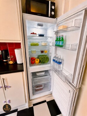 A kitchen with a microwave above the refrigerator, which is stocked with various food items and beverages. - Stylish 2-Bed Bedford Home | Sleeps 4 + Sofa Bed | Free Parking |Super Fast WiFi (Bedford)