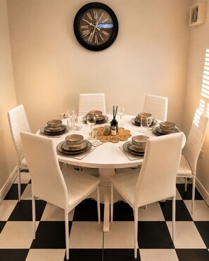 A round dining table with white chairs, set for a meal with plates, glasses, and a centerpiece. - Stylish 2-Bed Bedford Home | Sleeps 4 + Sofa Bed | Free Parking |Super Fast WiFi (Bedford)