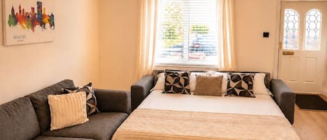 Une chambre à coucher comprenant un lit, un canapé, une œuvre d’art représentant un paysage urbain, un lustre et une porte avec des panneaux de verre.
