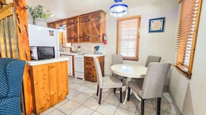 Cocina compacta con muebles de madera, microondas, estufa y una mesa de comedor con sillas.
