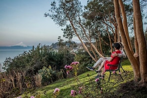 A person sitting on a bench with a view of a body of water and a mountain in the distance.