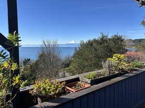 Een balkon met plantenbakken en uitzicht op zee en een berg.