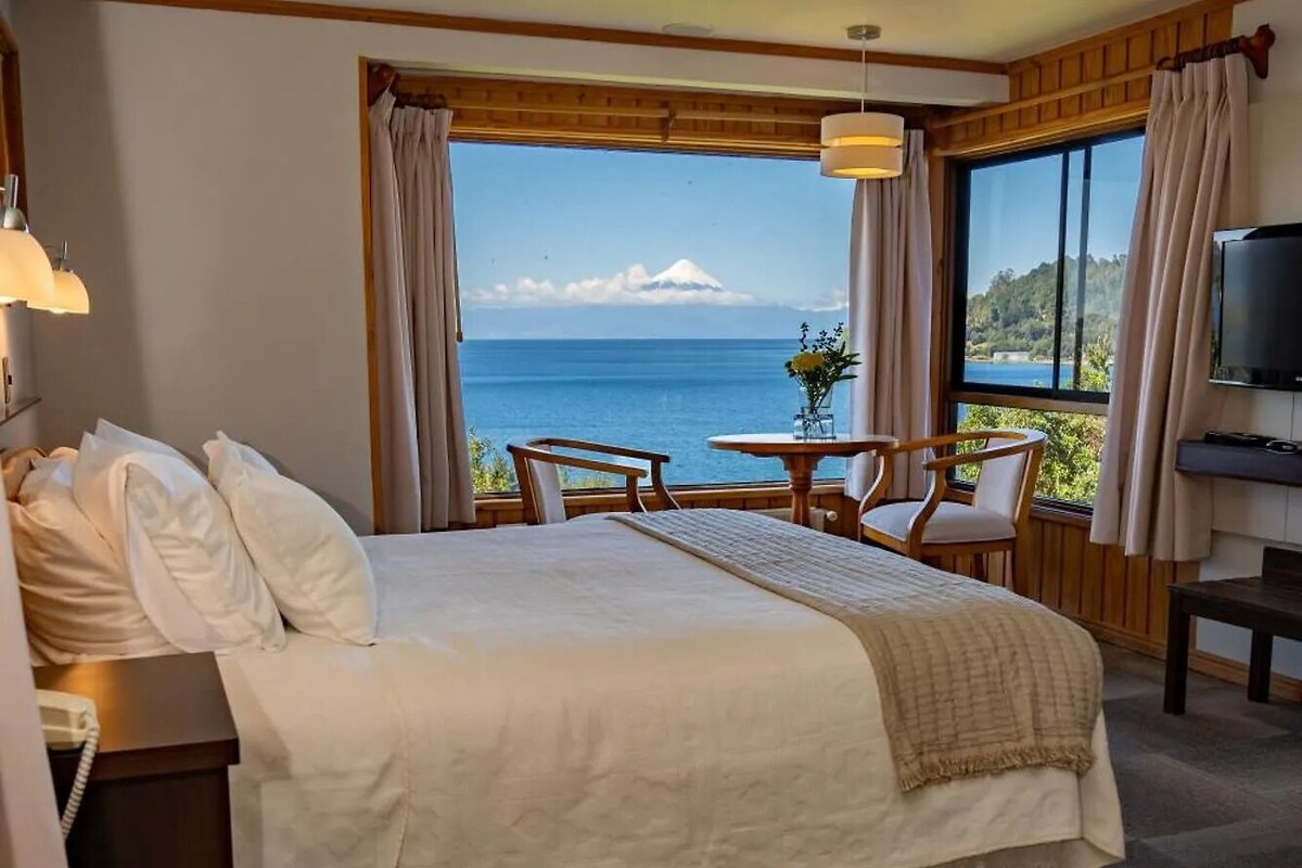 A hotel room with a bed, a desk with a telephone, a table with chairs, and a television.
