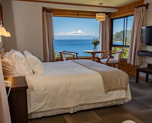 Una habitación de hotel con cama, escritorio con teléfono, mesa y sillas, y televisor.