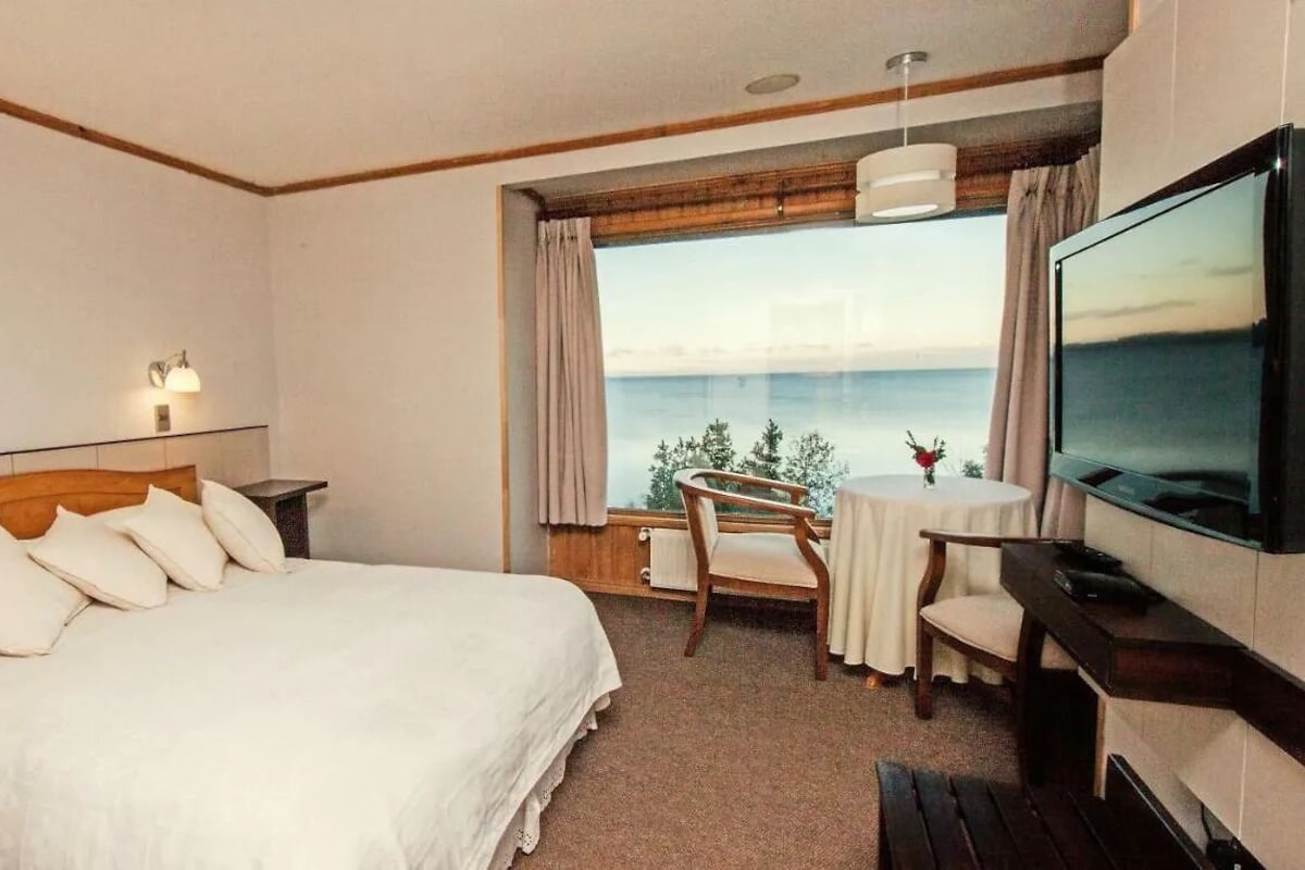 Habitación de hotel con cama, televisión, mesita y vistas al mar.