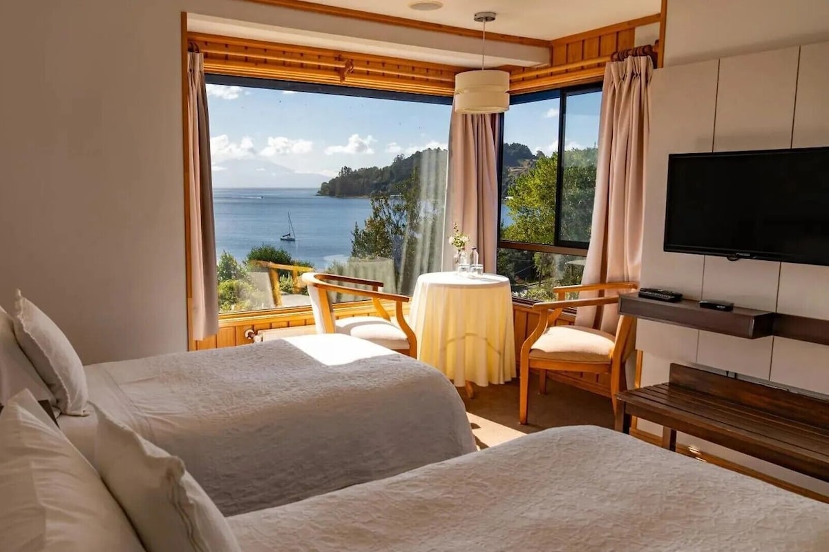 Habitación de hotel con dos camas, televisión, mesa y sillas, y vista al mar.