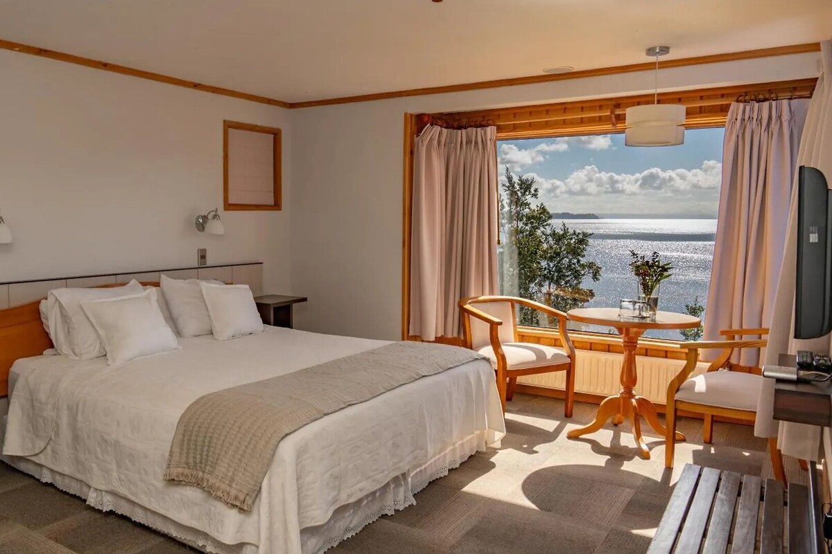 Habitación de hotel con cama, mesita de noche, lámpara y vistas al mar.