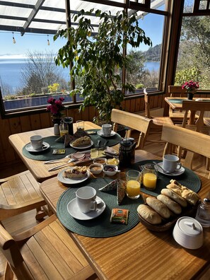 Una mesa de desayuno con diversos alimentos, una cafetera y vistas al exterior.