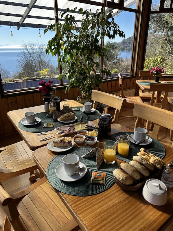 A breakfast table with various food items, a coffee pot, and a view of the outdoors.