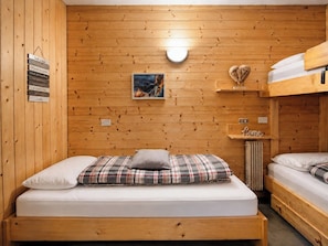 Ein Holzhüttenraum mit Etagenbett, Einzelbett, einer Wandleuchte, einem gerahmten Bild und einem Regal mit der Aufschrift 'Home'.