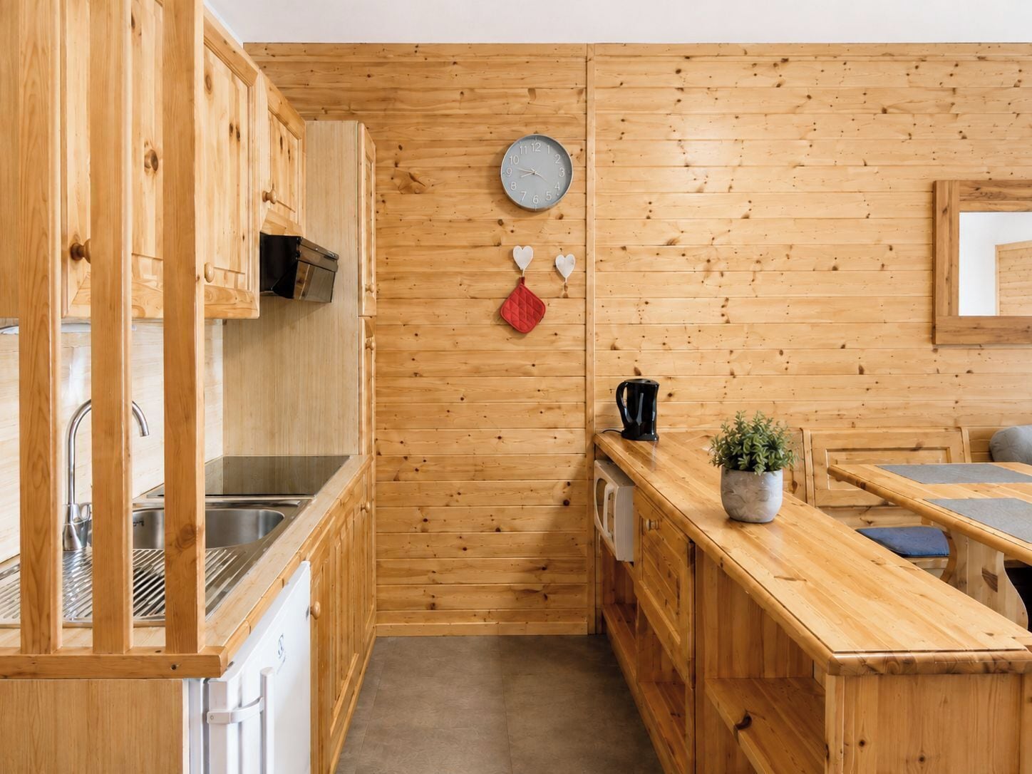 A compact kitchen with wooden cabinetry, a built-in stove, a sink, and a clock on the wall.