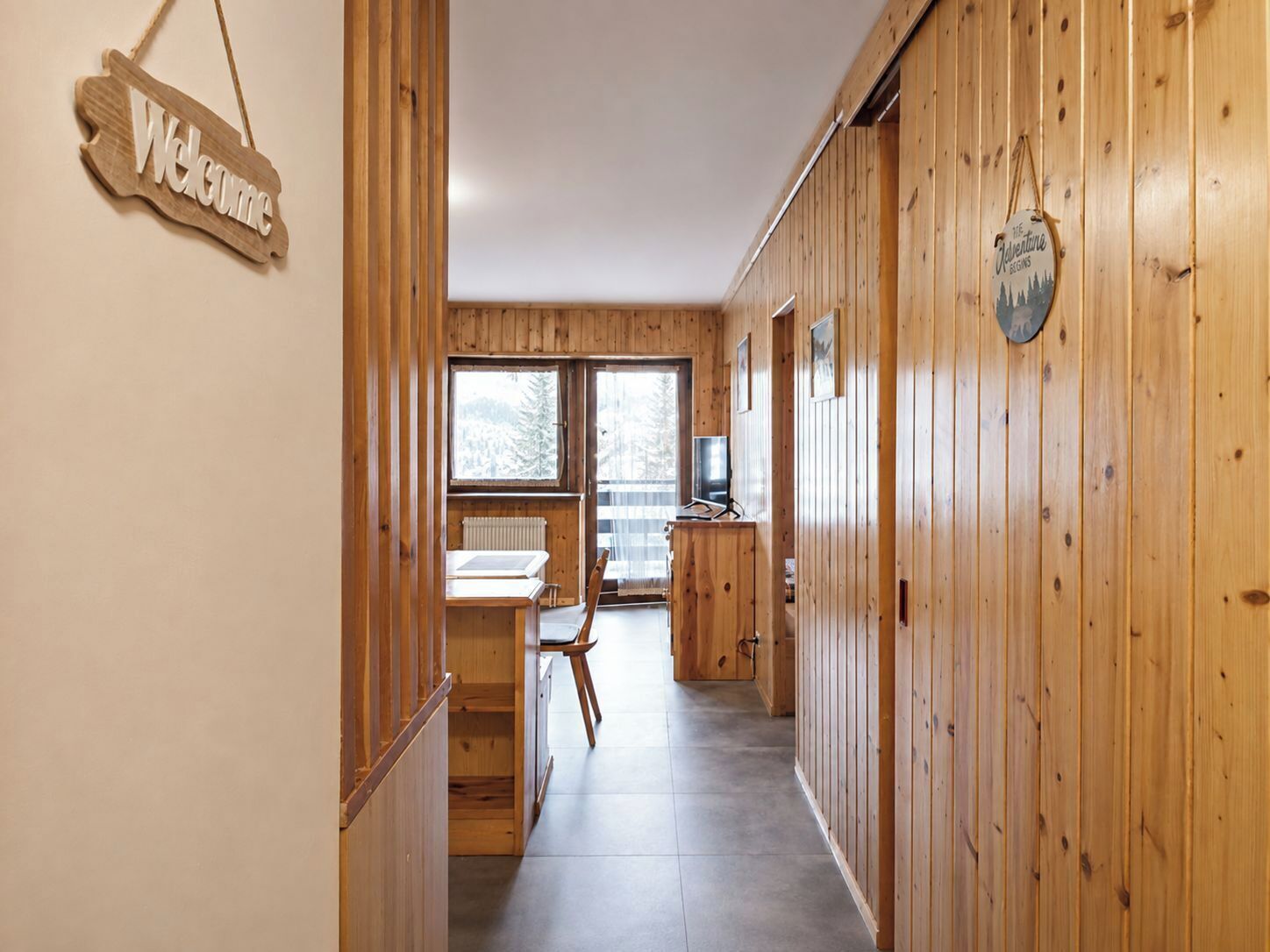 Interior de madera con un letrero que dice 'Welcome', un comedor y vistas a través de amplios ventanales.