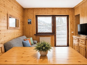 Ein Holzinterieur mit einer Couch, einem Esstisch, einer Zimmerpflanze und einem Fernseher.
