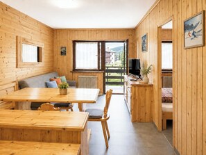A wooden interior with a dining table, chairs, a sofa, and a television on a wooden cabinet. - Casa Veronza - Residence Veronza with pool, sauna and baby club (Cavalese)