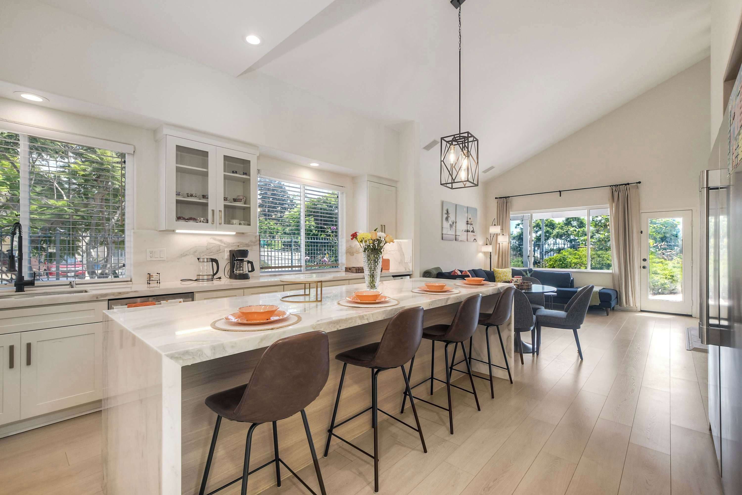 A modern kitchen with a central island, bar stools, and a dining area with a sofa.