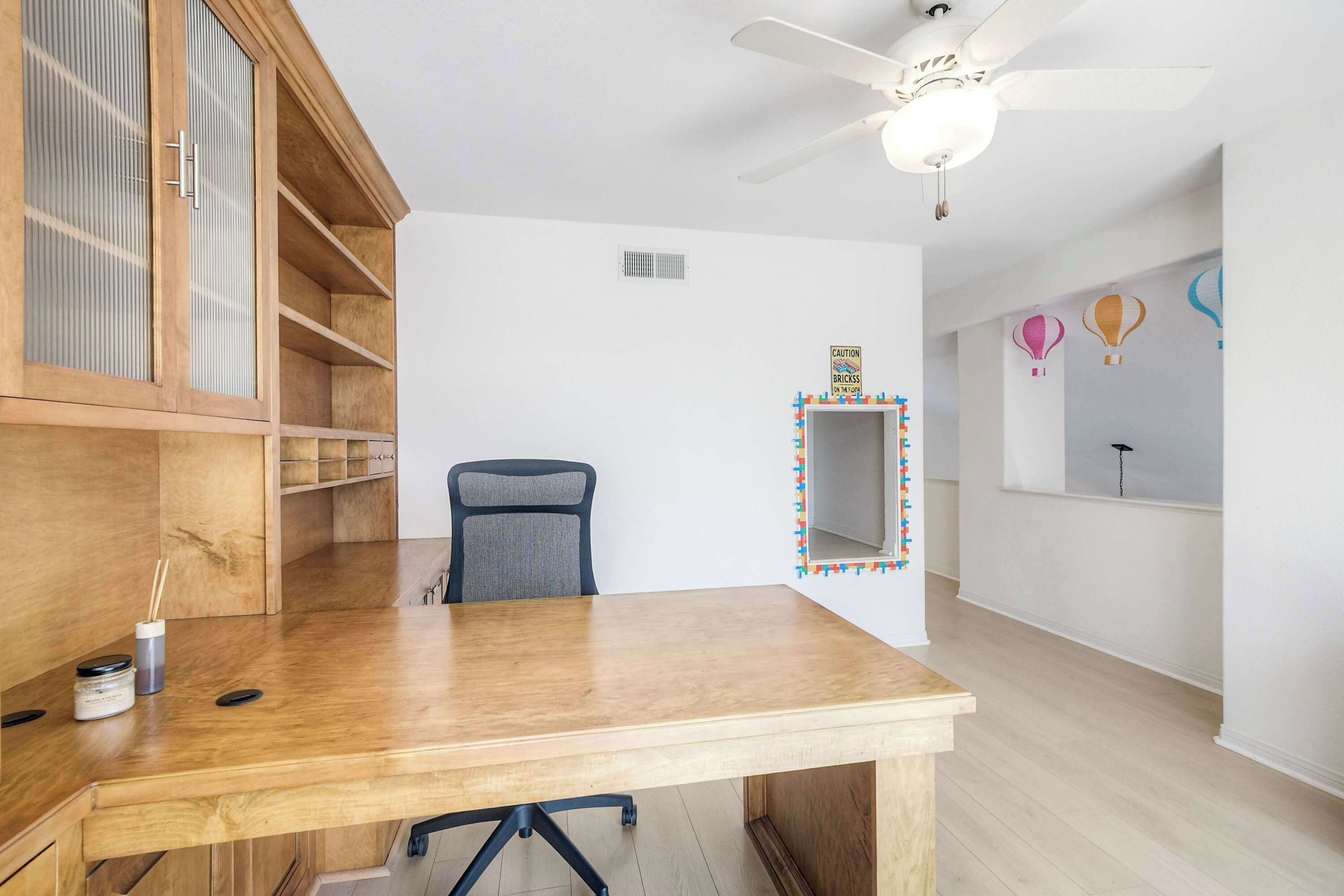 A room with a wooden desk, a chair, a ceiling fan, and a wall with a caution sign.