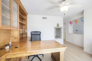 A room with a wooden desk, a chair, a ceiling fan, and a wall with a caution sign. - Brick & Beach Family Retreat (Carlsbad)