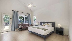 Ein Schlafzimmer mit einem großen Bett, einem Deckenventilator, einem Nachttisch und Blick durch das Fenster.