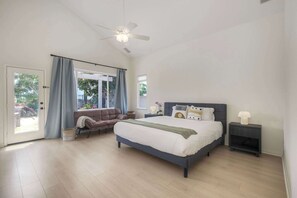 Quarto com uma cama grande, um ventilador de teto, uma mesa de cabeceira e vista pela janela.