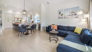 Ein modernes Wohnzimmer mit einem blauen Sofa, einem Essbereich mit Stühlen und einer Küche im Hintergrund.
