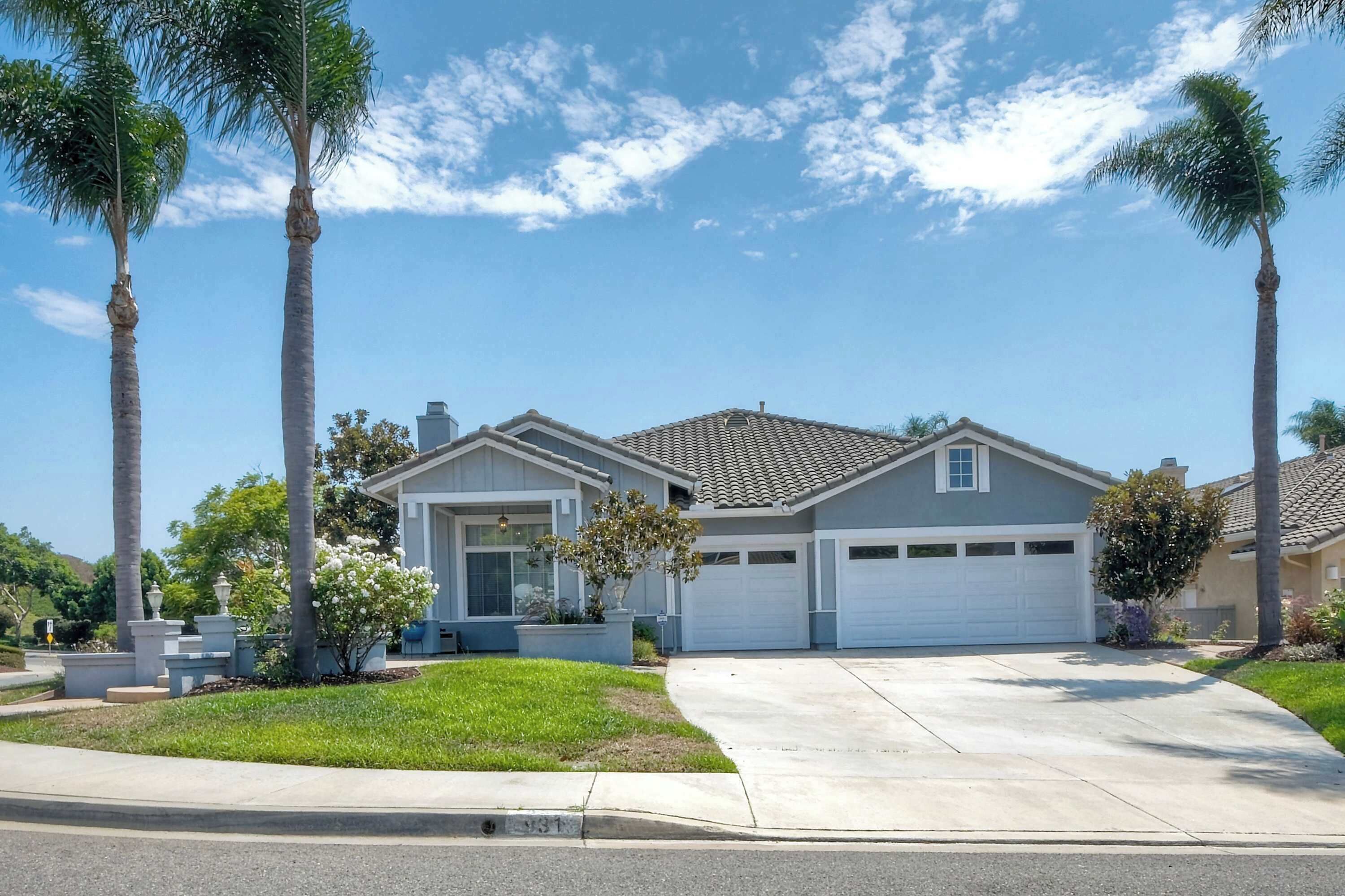 A residential house with a garage, surrounded by palm trees and a well-maintained lawn.