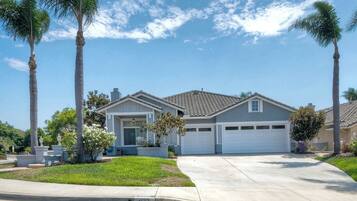 A residential house with a garage, surrounded by palm trees and a well-maintained lawn.