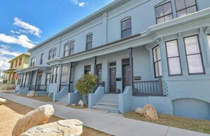 A row of blue two-story townhouses with front porches and steps leading to the entrance.