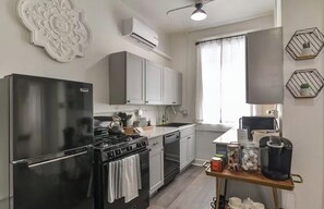 A modern kitchen with a black refrigerator, stainless steel appliances, white cabinets, and a wooden table with kitchenware. - Apartment in Historic Downtown Prescott - Fremont Room (Prescott)