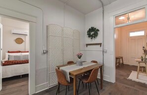A room with a dining table, chairs, a white partition, a bed with a red blanket, and a small table with a vase of flowers. - Apartment in Historic Downtown Prescott - Fremont Room (Prescott)
