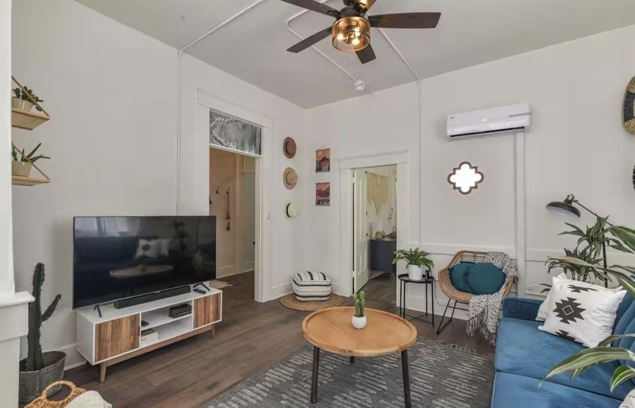 Uma sala de estar moderna com uma televisão de tela plana, um ventilador de teto, um sofá azul e uma mesa de centro.