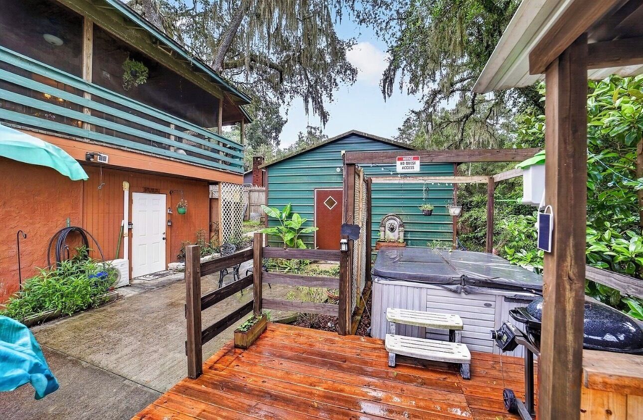 Eine Holzterrasse mit Whirlpool, überdachter Außenbereich zum Sitzen und ein eingezäunter Garten.