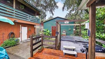 Eine Holzterrasse mit Whirlpool, überdachter Außenbereich zum Sitzen und ein eingezäunter Garten.
