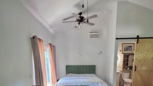 A room with a bed, a green sofa, a ceiling fan, and a wooden floor.