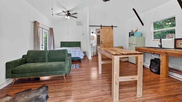 A room with a green sofa, a wooden table, a ceiling fan, and a window with a view of greenery.