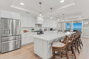A modern kitchen with a large island, stainless steel appliances, and a view to the outside. - Beach Flower 201 - Beautiful Beachfront Condo w/ Balcony, Elevator, & Beach Gear. (Madeira Beach)