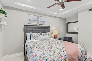 Ein Schlafzimmer mit einem Bett, einem Deckenventilator, einem Nachttisch mit Lampe und zwei gerahmten Bildern an der Wand.