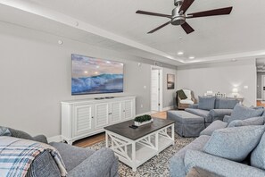 Ein modernes Wohnzimmer mit Deckenventilator, großem Wandfernseher und einer Sitzecke mit Sofas und Couchtisch.