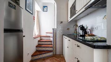 Una cucina con mobili bianchi, un frigorifero in acciaio inossidabile, una parete rivestita di piastrelle e un piano di lavoro nero.