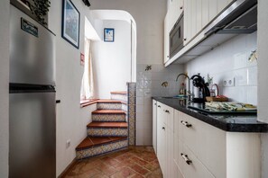 Cozinha com armários brancos, geladeira de aço inoxidável, painel de azulejos e bancada preta.