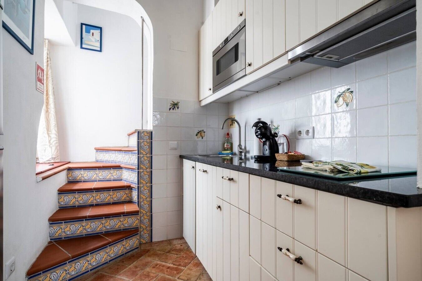 Cocina con gabinetes blancos, encimera negra y salpicadero de azulejos.