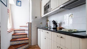 Cucina con mobili bianchi, un piano di lavoro nero e una parete piastrellata.