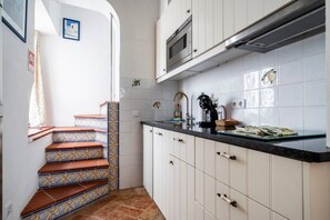 Een keuken met witte kasten, een zwart aanrecht en een betegelde spatwand.
