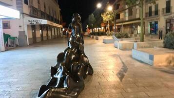 Une sculpture se trouve sur une place publique, avec des bâtiments en arrière-plan.