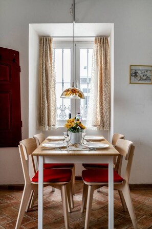 Un coin repas avec une table dressée pour deux personnes, un vase rempli de fleurs jaunes et une porte rouge.