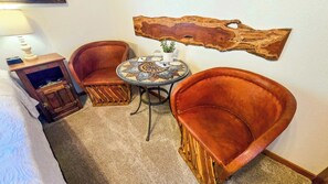 Una habitación de esquina con una mesa redonda, dos sillones de cuero, un mueble pequeño y un adorno de madera en la pared.