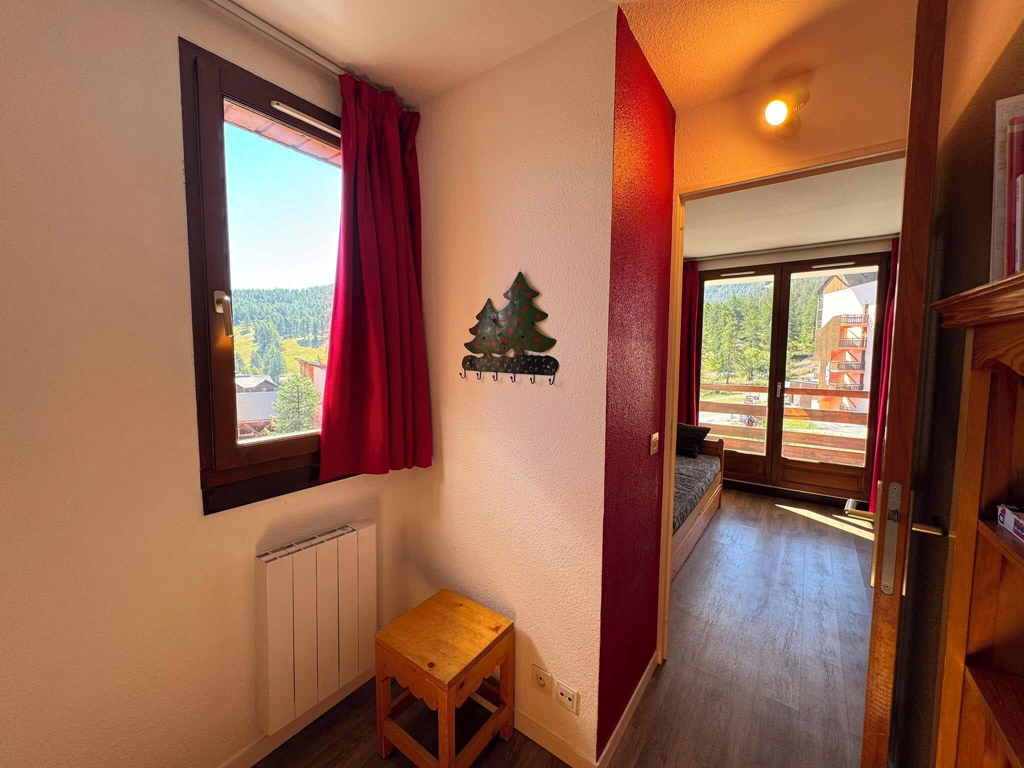 Een gang met een houten bankje, een radiator, een kerstversiering aan de muur, en uitzicht op een gebouw door een raam.