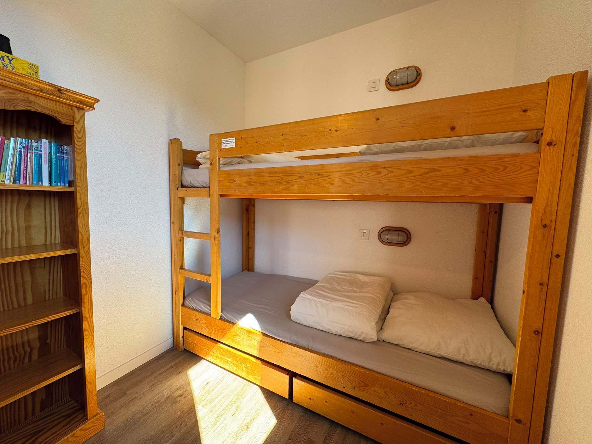A bunk bed with a wooden frame, a shelf unit with books, and a small window.