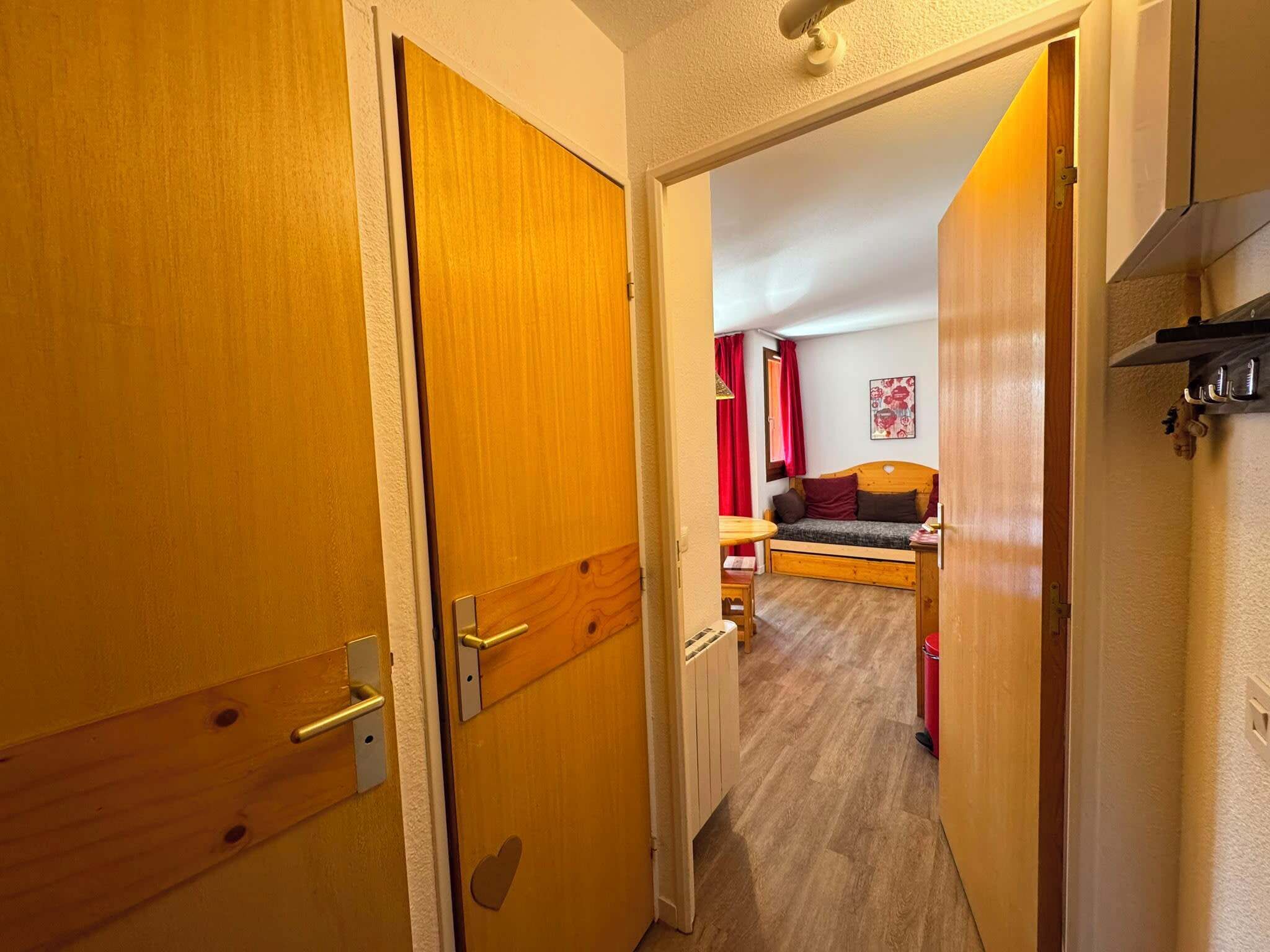 A hallway leading to a bedroom with a bed, a small table, and a red curtain.