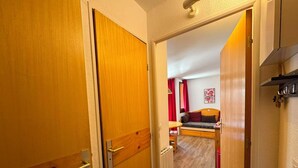 A hallway leading to a bedroom with a bed, a small table, and a red curtain.